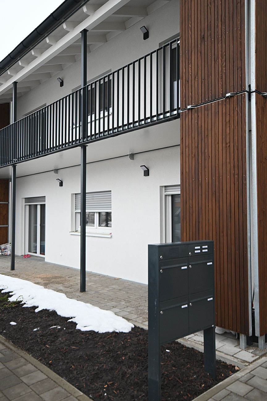 Detailansicht der Fassade des Mehrfamilienhauses mit Holzverkleidung, umlaufendem Laubengang und Briefkastenanlage im Außenbereich.