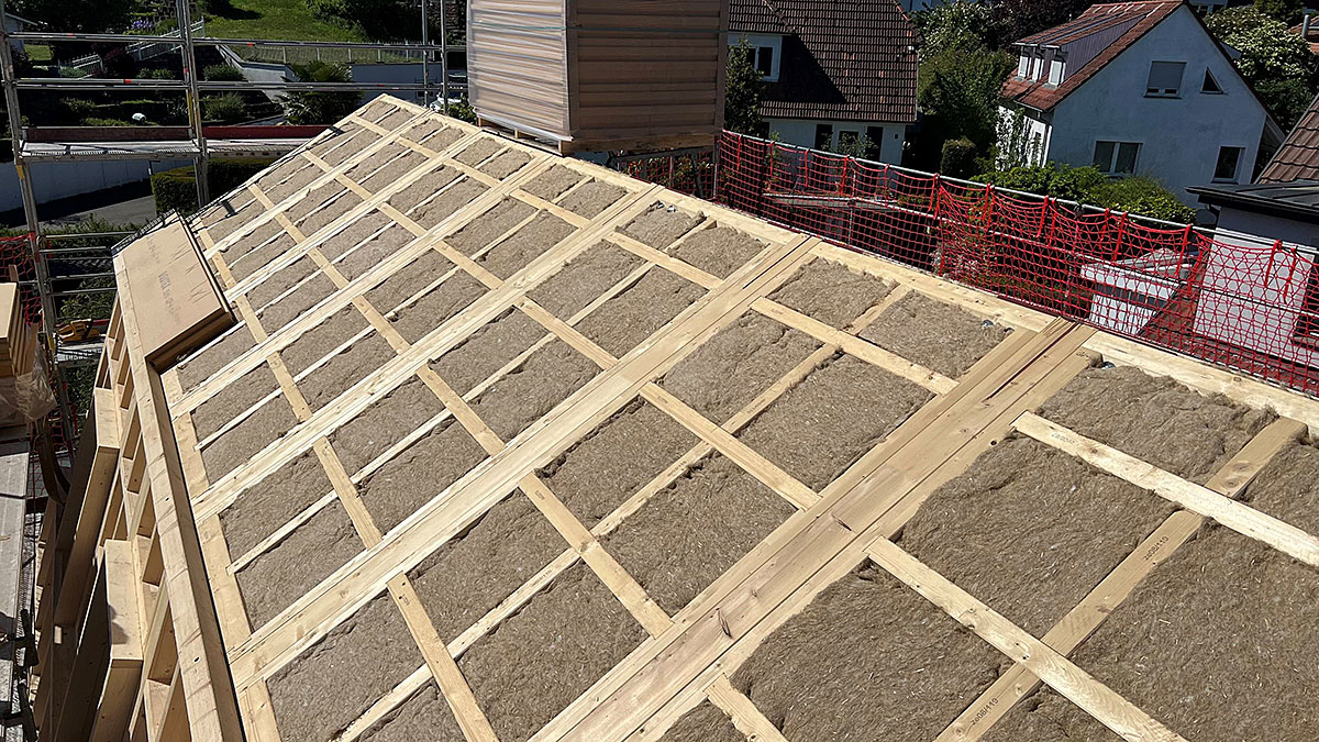 Geneigtes Hausdach im Bau mit zwischen Holzlatten verlegter Dämmung und vorbereiteter Unterkonstruktion für die Dacheindeckung.
