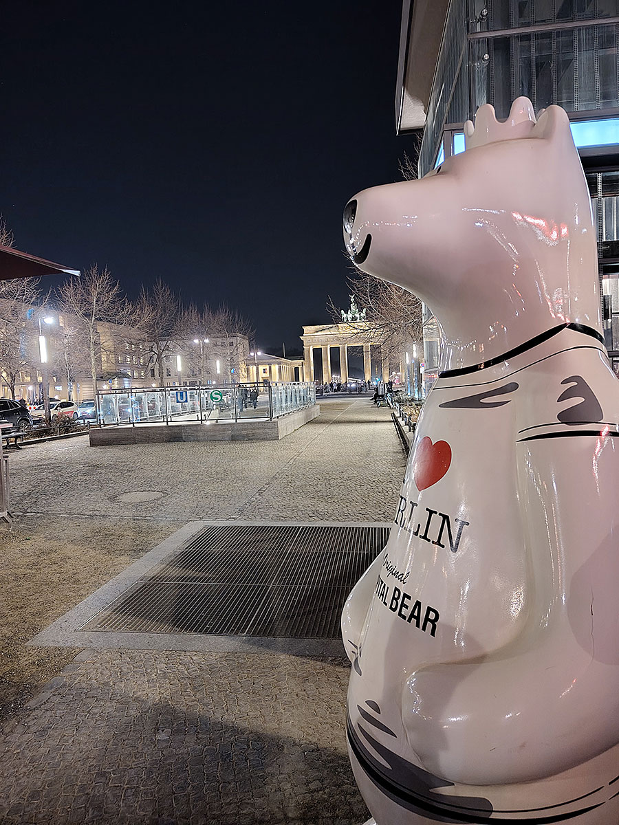 Große weiße Buddy-Bären-Skulptur mit der Aufschrift „I ♥ Berlin“ auf einem Platz nahe dem Brandenburger Tor bei Nacht.
