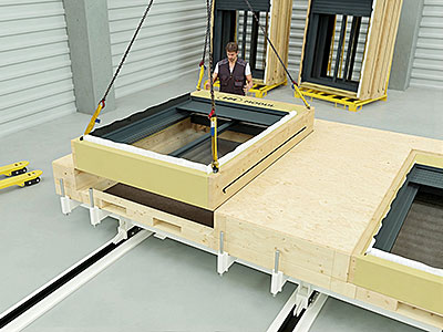 Vorgefertigtes Fenstermodul wird mit Hebevorrichtung in eine Holzdecke eingesetzt; eine Person überwacht die präzise Positionierung in einer Werkhalle.