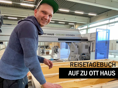 Person mit grüner Kappe lehnt an einer Holzrahmenkonstruktion in einer Produktionshalle; im Hintergrund ist eine Fertigungsanlage von „OTT HAUS – Gesund wohnen“ zu sehen. Eingeblendeter Text: „Reisetagebuch – Auf zu OTT Haus“.