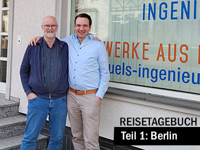 Zwei Personen stehen nebeneinander vor einem Schaufenster mit der Aufschrift eines Ingenieurbüros. Unten im Bild steht der Titel „Reisetagebuch – Teil 1: Berlin“.