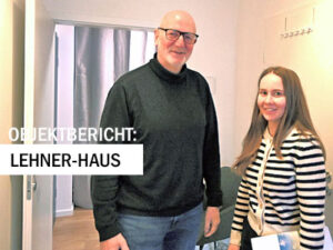 Zwei Personen stehen lächelnd in einem Büro oder Beratungsraum. Über dem Bild steht der Hinweis ‚Objektbericht: Lehner-Haus‘.